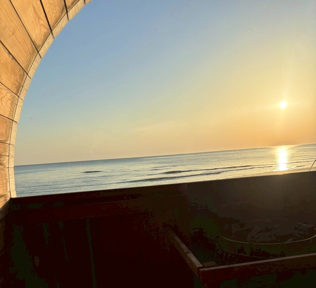 バレルサウナの丸い窓から見た、日本海に沈む夕日